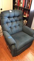 Full view of the blue rocking recliner chair showing padded tufted back, cushioned armrests, and fabric upholstery with pet hair visible.