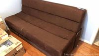 Front side view of brown fabric futon sofa bed showing seat and back cushions with some pet hair visible.