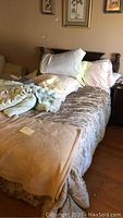 Full view of bed made with floral bedspread, beige blanket, multiple pillows, and linens showing assorted bedding items on bed and nearby.