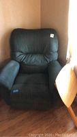 Photo of dark green recliner chair with upholstered cushions and padded arms against a beige wall.