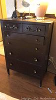 Full view of brown wooden dresser with drawer pulls and top items.