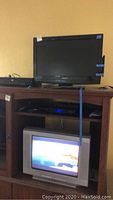 Magnavox 26-inch TV on top of wooden entertainment center with Apex DVD player next to it, Sony Trinitron TV visible below showing image on screen.