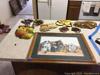 Table with framed watercolor painting and multiple vintage kitchen wall decor pieces arranged on it.