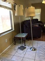 Two metal floor lamps positioned near a window and sofa, with clear view of bases and embroidered shades.