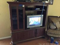 Media center showing front with TV in center and glass door shelves on left, with wooden cabinets below.