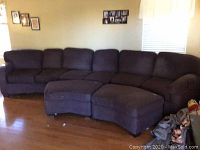 Full view of curved sectional sofa with two ottomans in living room setting, showing overall shape and condition.