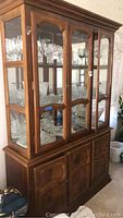 View of the wood hutch with glass front doors and interior shelving displaying glassware, highlighting the overall structural condition and style.