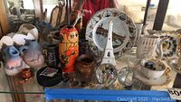 Glass shelf display of Limoge Eiffel Tower figurine, painted pottery, travel plates, stacking doll, and glass paperweights