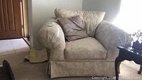 Front angled view of the beige floral patterned oversized armchair with one gray pillow on it.