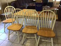 Four wooden kitchen chairs with white painted frames and natural wood seats arranged indoors on a tiled floor.