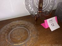 Close-up of a single clear Depression glass plate showing scalloped edges and floral etched pattern on the rim placed on wooden surface.
