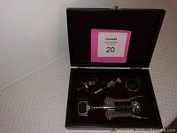 Five-piece wine tool set displayed in an open rosewood box with molded slots filled with corkscrew, stoppers, drip collar, and bottle opener.