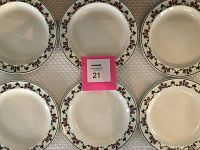 Top-down view of six round white plates with floral and vine border pattern around edge.