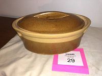 Photo showing the top and side view of the ceramic oval Dutch oven with tan glaze and molded handle on the lid.