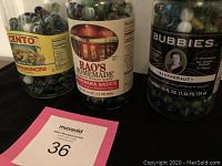 Three glass jars labeled Cento, Rao's Homemade, and Bubbies Sauerkraut filled with various marbles.