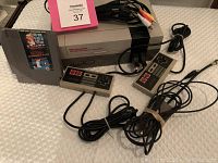 Full view of NES console, two wired controllers, AV cable, and game cartridge 'Super Mario Bros Duck Hunt'.