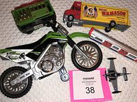 Photo showing Kawasaki dirtbike toy, green train car, red and yellow box truck, red and white train car, and small gray airplane toy on quilted background.