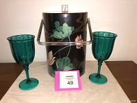 Front view showing black retro ice bucket with vinyl lily pad pattern, metal handle, clear lid, and two teal green ribbed wine glasses.
