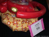 Red child's steering wheel toy with patterned yellow fabric base, showing condition and design details.