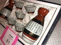 View of the sake set inside the original box showing the bottle and six cups with colorful bands and calligraphy.