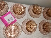 Overhead image showing all seven pink depression glass cups positioned on matching saucers, arranged in rows on a light surface.