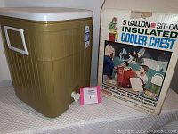 Vintage 5 gallon avocado green sit-on insulated cooler with white lid and spigot, shown with original box featuring 70's style images