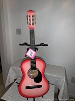 Full view of the faded pink acoustic guitar on stand, showing body and neck.