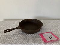 Antique cast iron pan size 5 with handle and visible pour spouts, placed on white quilted surface, with lot number card.