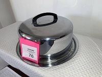 Closed vintage locking cake pan with black handle on the cover, shiny metal with reflections, showing a locking clasp on the base.