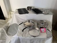 Overview of miscellaneous pots, pans, including large oval silver tray, lidded frying pan, cooling racks, and egg poacher pan