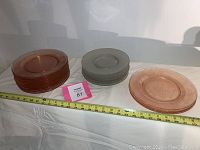 Shows stacks of pink plates on the left and clear crackle plates on the right with a measuring tape indicating size.