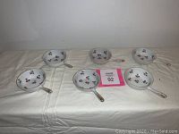 Front view of six white handled porridge dishes featuring small red floral patterns laid out on a light-colored surface.