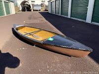 Side view of the canoe showing interior seating and paddle inside, worn condition with black paint on bow and edges.