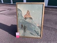 Full view of framed vintage mountaineering skiing picture print showing two men climbing snowy mountain with peak in background.