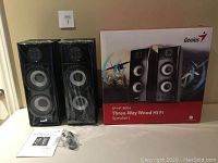 Pair of black Genius SP-HF1800A speakers with factory wrap, manual, cables, and original box featuring product art and branding.