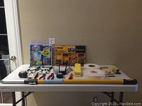 Photo showing full array of tools and supplies on table including DeWalt 58 piece screwdriving set, Windex window washing set, Stanley gloves, drywall tape, extension pole, pole sander and hand tools.