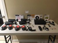 Full view of lot including 4 Defender cameras, DVR unit, cables, remote, mouse, software CD, power adapter, and manuals on a white table