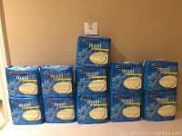 11 sealed blue packages of Exact Maxi Pads Regular, stacked in two rows showing front packaging with logo and product details.