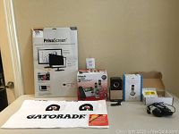 Full view of lot items on table: VTech phone system box, PrivaScreen package, AT&T handset box, Skinny Dip speaker, Gatorade towel, Plantronics headset.