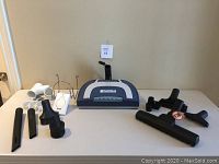 Central vacuum power head model Kenmore SKM100 on a table with multiple vacuum attachments around it.
