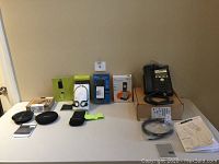 Overview of the lot items on a table including speakerphone, headphones, surge protector, telephone handsets, cables, and boxes