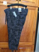 Side view of black capris with dark floral pattern hanging on hanger, tags still attached