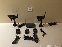 Photo of two black Defender Phoenix Pro wireless cameras with antennas and cables, wireless receiver, three power adapters, and assorted cables on table.