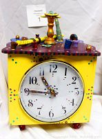 Front view of square yellow wooden clock with whimsical painted accents and clock face showing 10:43.