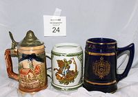 Photo shows all three beer steins lined up: German pewter lid stein on left with scenic house, white stein with knight in center, US Navy dark blue stein on right.