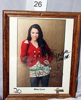 Framed autographed photo of Miley Cyrus in a red cardigan with her autograph and message written on the photo.
