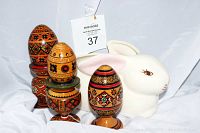 Three Ukrainian Pysanky decorative wooden eggs on stands in front of a white porcelain bunny planter.