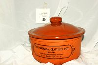 Brown glazed clay pot with lid featuring black printed text and decorative motif on front.