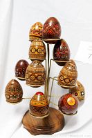 Close-up photo showing detailed hand painted patterns on wooden eggs arranged on the wire holder attached to a wood base.