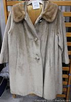 Front view of beige vintage women's fur coat with mink collar and gold satin lining, displayed on a wooden backdrop.